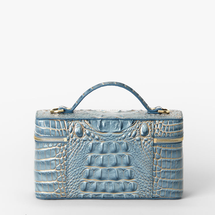 A light blue crocodile-embossed leather cosmetic case with a top handle, gold-tone zipper, and a small gold Brahmin plaque on the front, set against a plain white background. Back view.