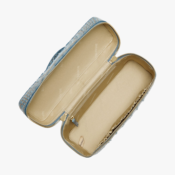 A light blue monogram-patterned zippered handbag shown open, revealing a beige interior lining with the brand name 'Brahmin' printed repeatedly.