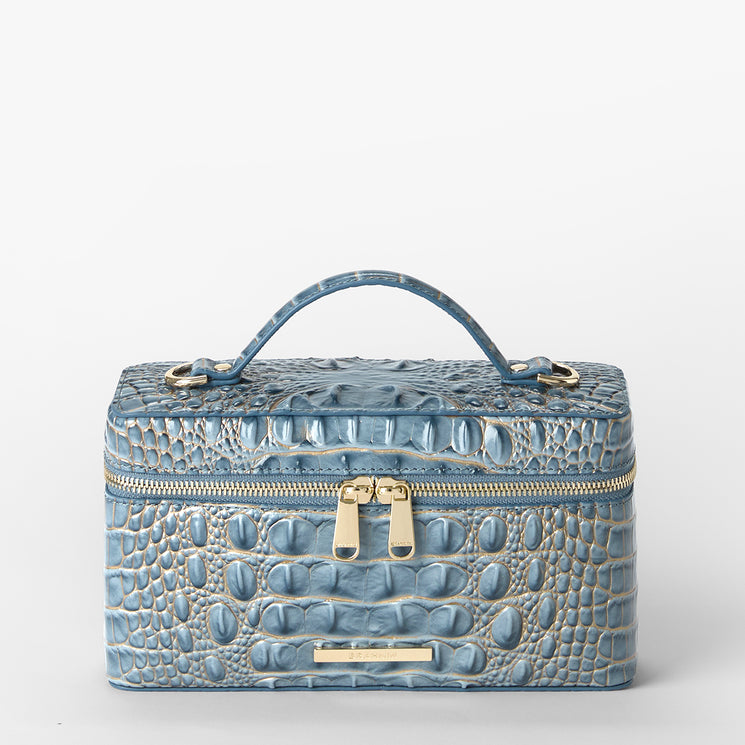 A light blue crocodile-embossed leather cosmetic case with a top handle, gold-tone zipper, and a small gold Brahmin plaque on the front, set against a plain white background.