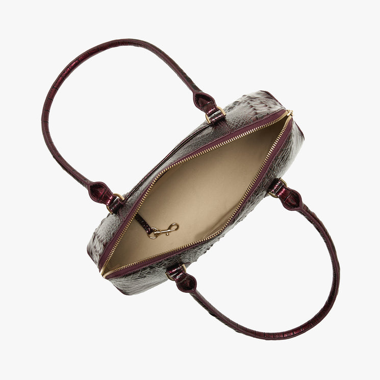 An open top view of a snakeskin-patterned handbag with a burgundy leather handle and gold-tone zipper, showing a beige interior, on a light gray background.