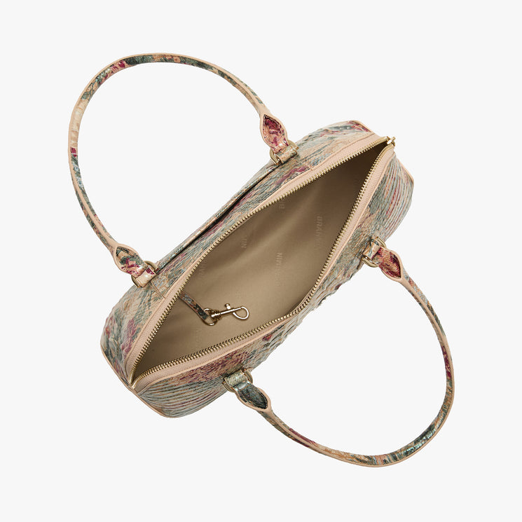 An open top view of a structured handbag with a muted floral pattern in beige, pink, and green, featuring a light beige interior and gold-tone hardware, set against a plain light gray background.