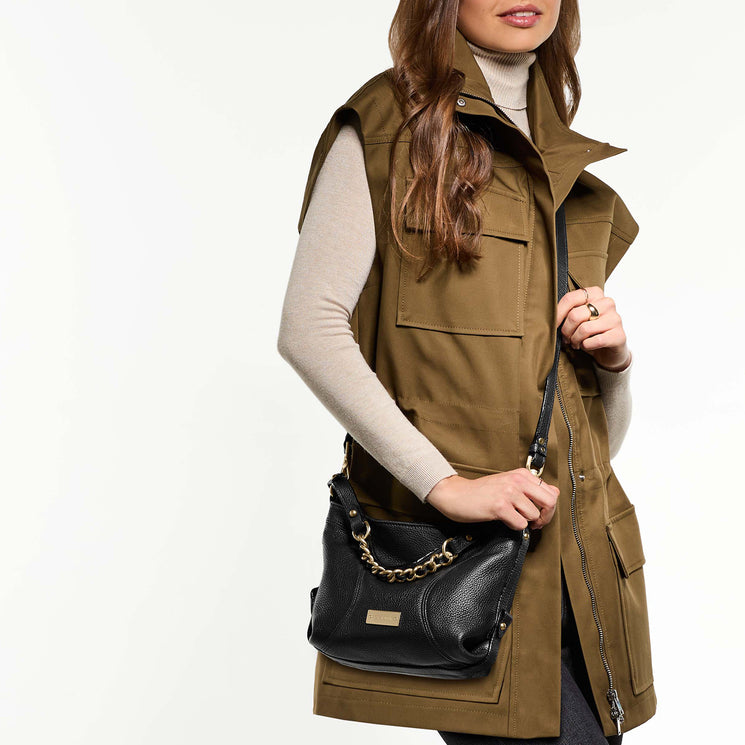 Woman wearing a brown vest holding Small Hailey crossbody on a white background