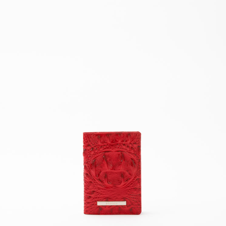 BRAHMIN Travel Pouch Set in vibrant red stands upright against a white background, featuring embossed circular patterns, a small metallic BRAHMIN logo plate, and rectangular silhouette; no straps visible.