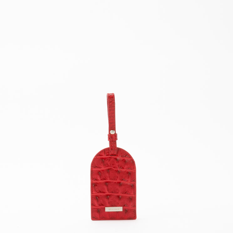 BRAHMIN Travel Pouch Set featuring a red, textured luggage tag with embossed crocodile-inspired pattern, metal nameplate, attached buckle strap; all upright on a white background.