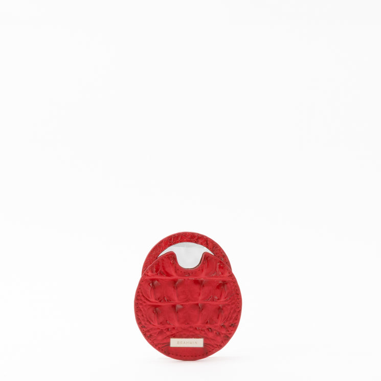 BRAHMIN small round travel pouch in vibrant red with textured surface, silver-tone clasp closure, and metallic logo plate at bottom center. Pouch is displayed upright on a clean white background.