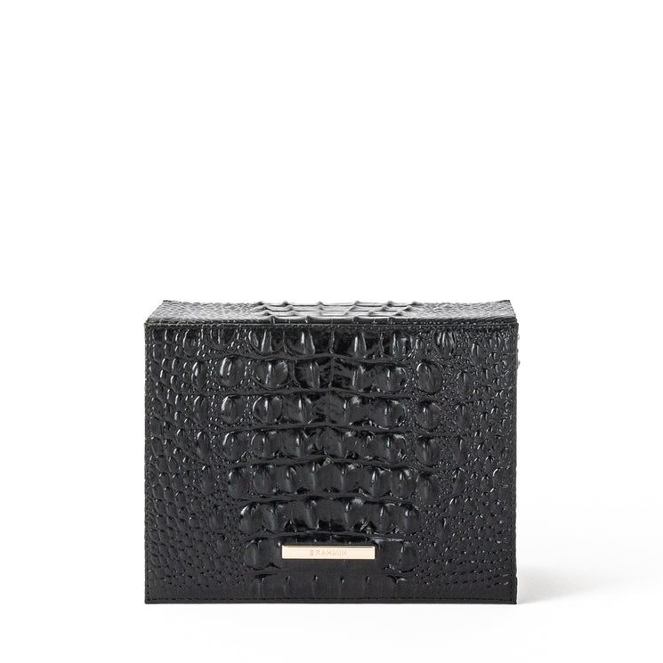 BRAHMIN Small Box bag in black embossed leather with a metallic brand label, structured silhouette, boxy shape, and top handle. Shown against a white background highlighting its luxe texture and details.