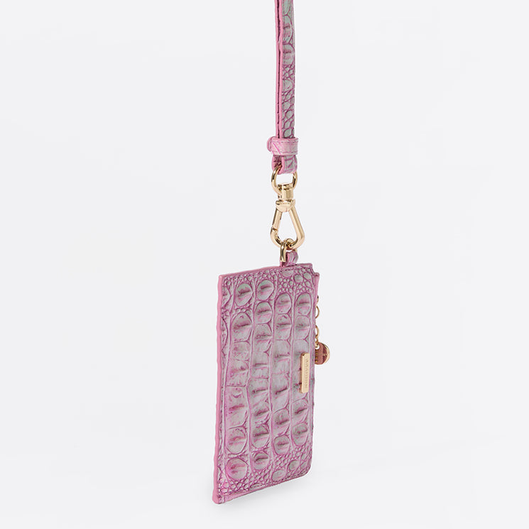 Brahmin pink textured wristlet with gold clasp, slim cardholder silhouette, and embossed pattern. Stands upright against a white background. Features a compact shape with visible top hardware and sleek design.