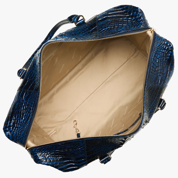 An overhead view of a blue crocodile-embossed leather bag, showing its beige interior lining and gold-tone hardware against a white background.