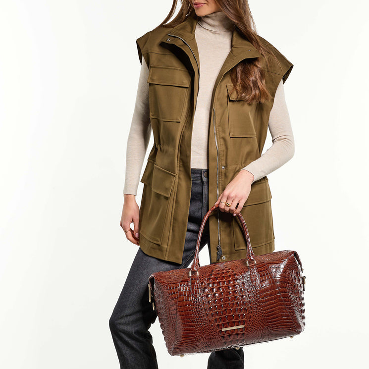 Person wearing a green vest holding Daniela travel bag on a white background