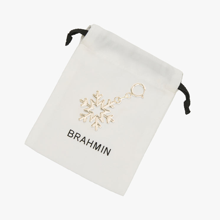 Gold-tone small snowflake charm with a lobster claw clasp, displayed on a small white fabric drawstring pouch featuring the Brahmin logo.