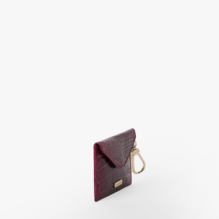 BRAHMIN Lana small pouch in burgundy with a textured envelope silhouette and gold keyring hardware, shown on a white background. The compact accessory features a chic, structured design ideal for clipping onto bags.
