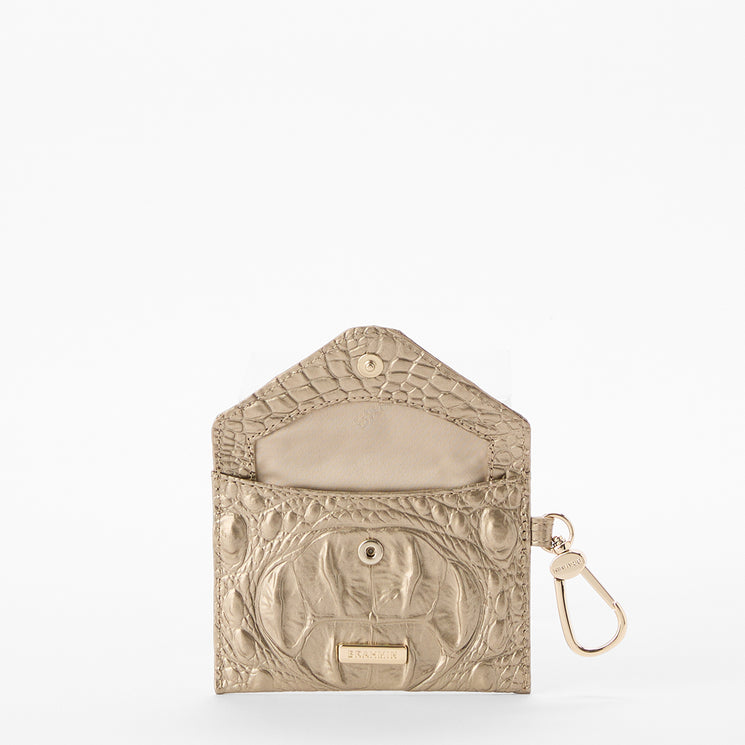 BRAHMIN Lana gold textured leather envelope pouch with snap closure, metal logo plate, and right-side key clip; chic clutch silhouette shown on a white background.