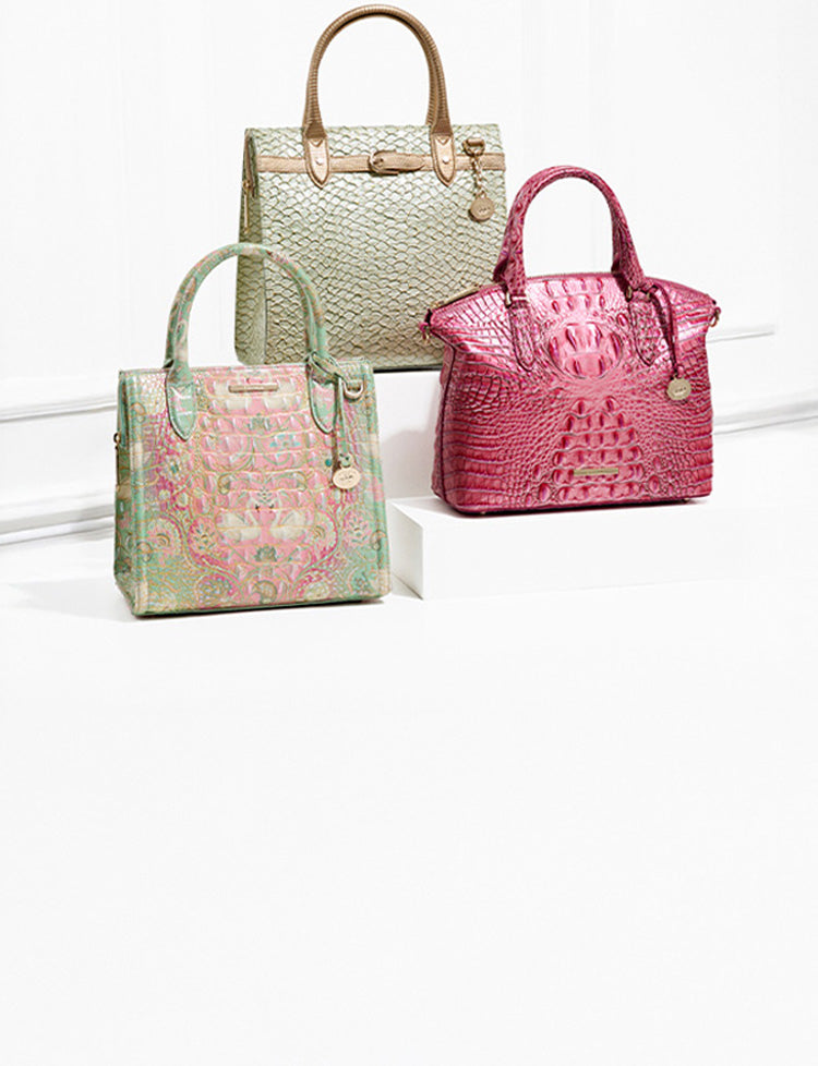 Three Brahmin handbags displayed against a white backdrop: a pastel green and pink embossed satchel, a vibrant hot-pink croc-embossed tote, and a light gold-green textured structured bag with tan handles.