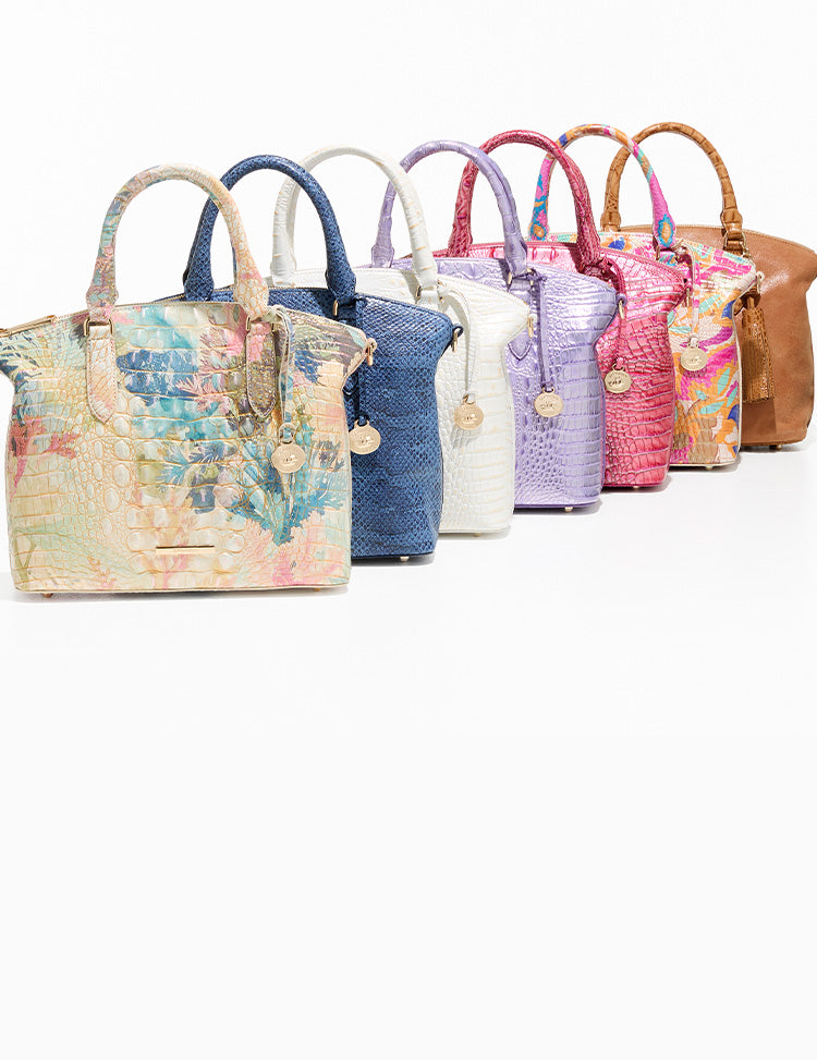 Seven Brahmin satchel handbags displayed side by side in assorted colors and textures including floral print, blue, white, lavender, pink, multicolor, and tan