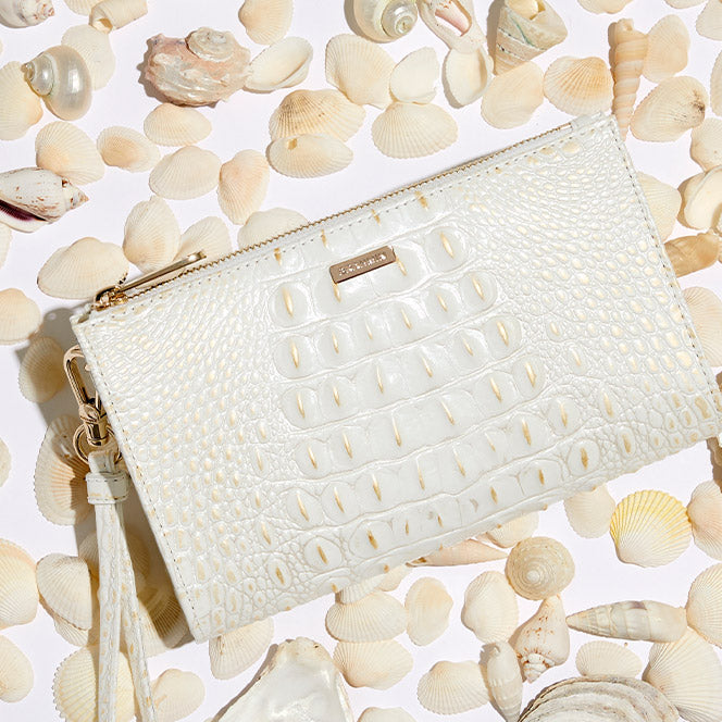 White croc-embossed leather wristlet with zip-top closure, detachable strap, and tassel zipper pull, styled on seashells