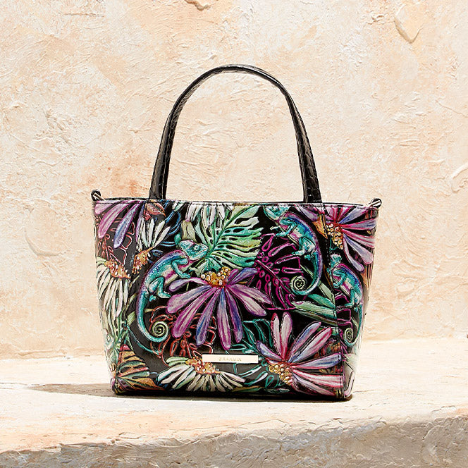 Black Brahmin tote with colorful tropical floral and chameleon print on a stone backdrop