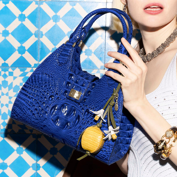 Blue Brahmin croc embossed leather shoulder bag with rounded silhouette, braided top handles, flap detail, gold hardware, and bag charms