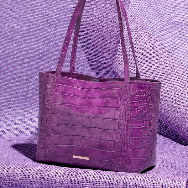 Purple croc embossed leather tote bag styled against textured purple fabric for a bold monochromatic handbag image.
