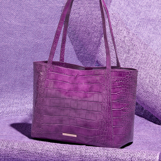 Purple croc embossed leather tote bag styled against textured purple fabric for a bold monochromatic handbag image.