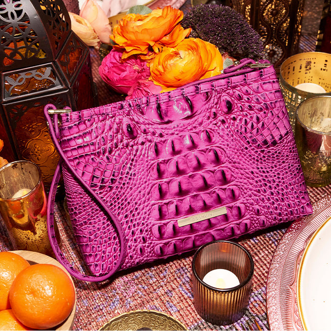 Bright pink Brahmin croc embossed leather zip pouch with slim shoulder strap, gold logo plaque, and glossy textured finish