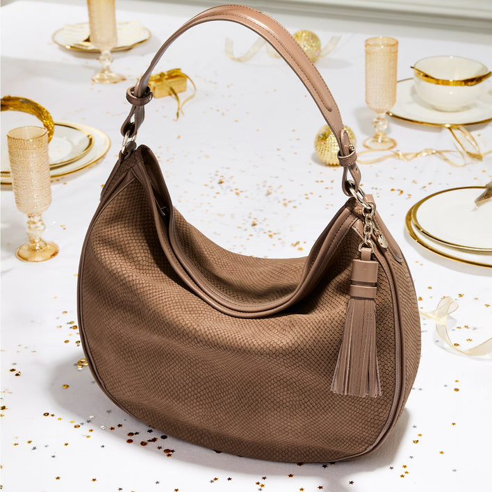 Brahmin hobo-style shoulder bag in taupe textured leather displayed on a white holiday table with gold-rimmed plates and confetti.