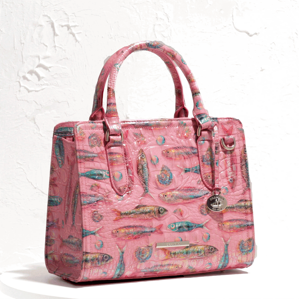 A Brahmin satchel in pink crocodile embossed leather featuring a colorful repeating illustration of tropical fish and seashells.