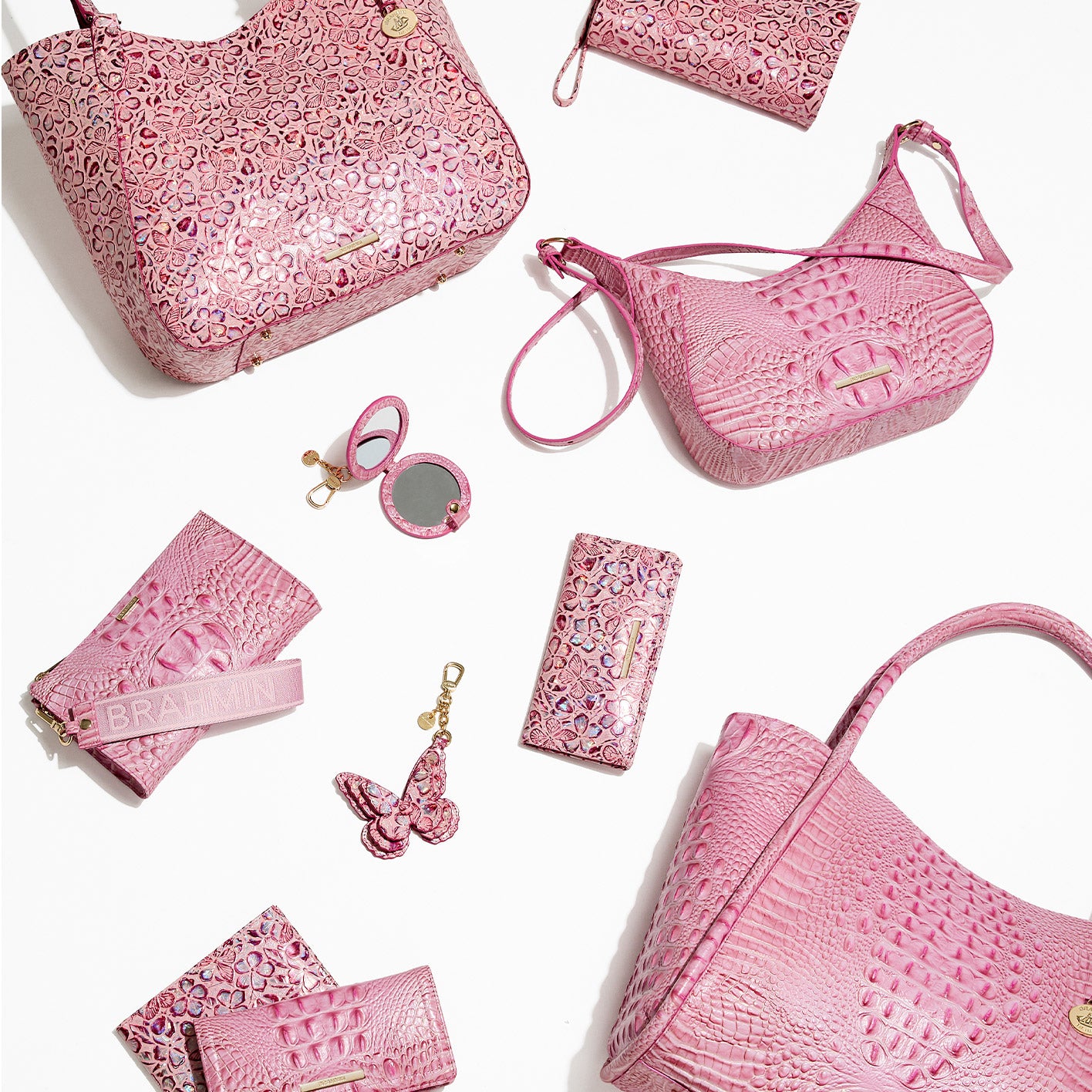 Brahmin Fearless Collection displayed on white background, featuring pink croc-embossed leather handbags, crossbody bag, tote, wallets, keychain, butterfly charm, and round mirror case. Ten percent of purchase price supports National Breast Cancer Foundation Inc.® through 10/31.