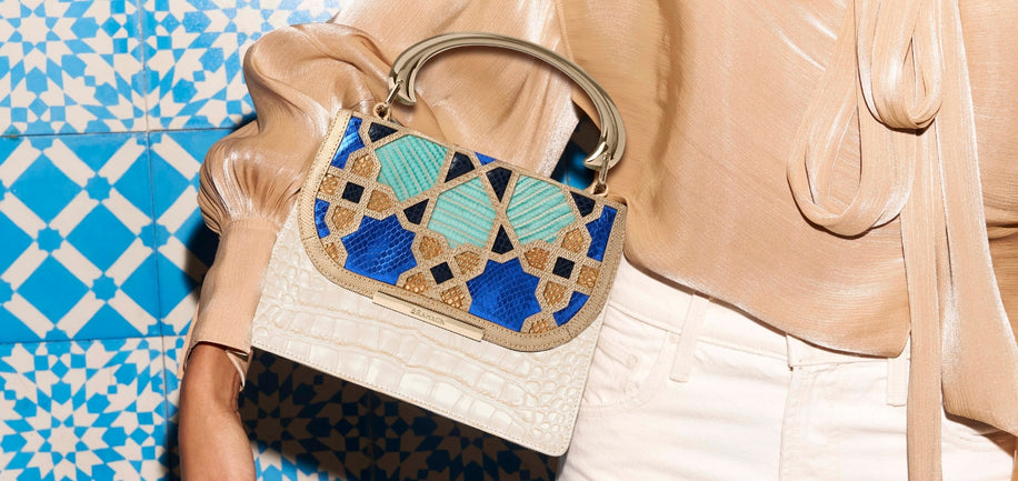 Person holding a decorative handbag with blue and green accents against a patterned background