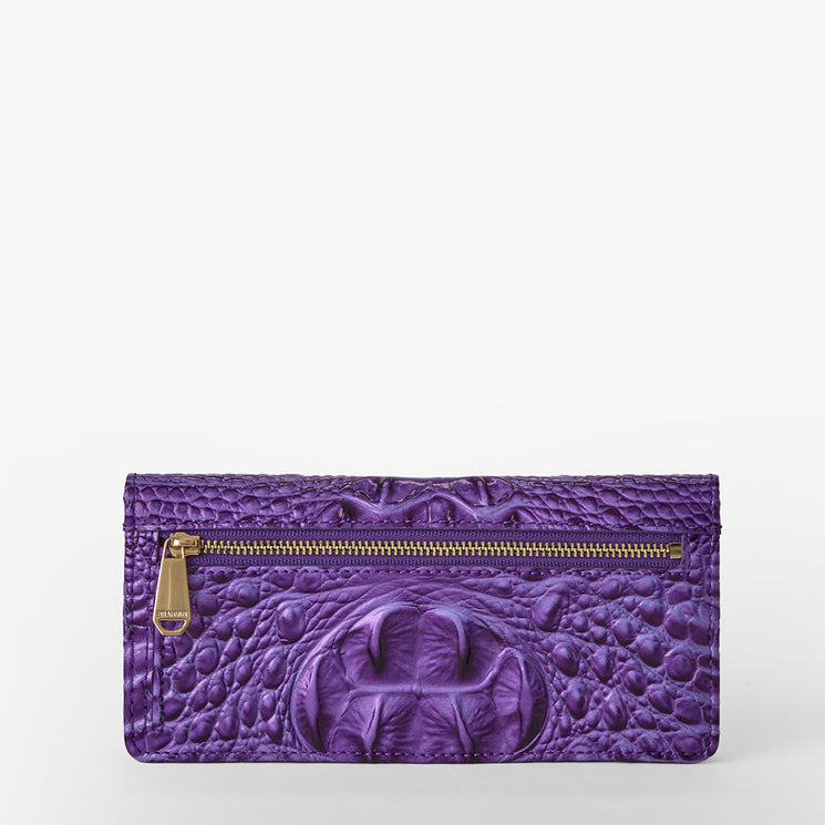Brahmin purple textured leather wallet with gold-tone zipper pocket on front, embossed crocodile-inspired pattern, raised oval detail at center. Front view highlighting color, hardware, and distinctive silhouette.