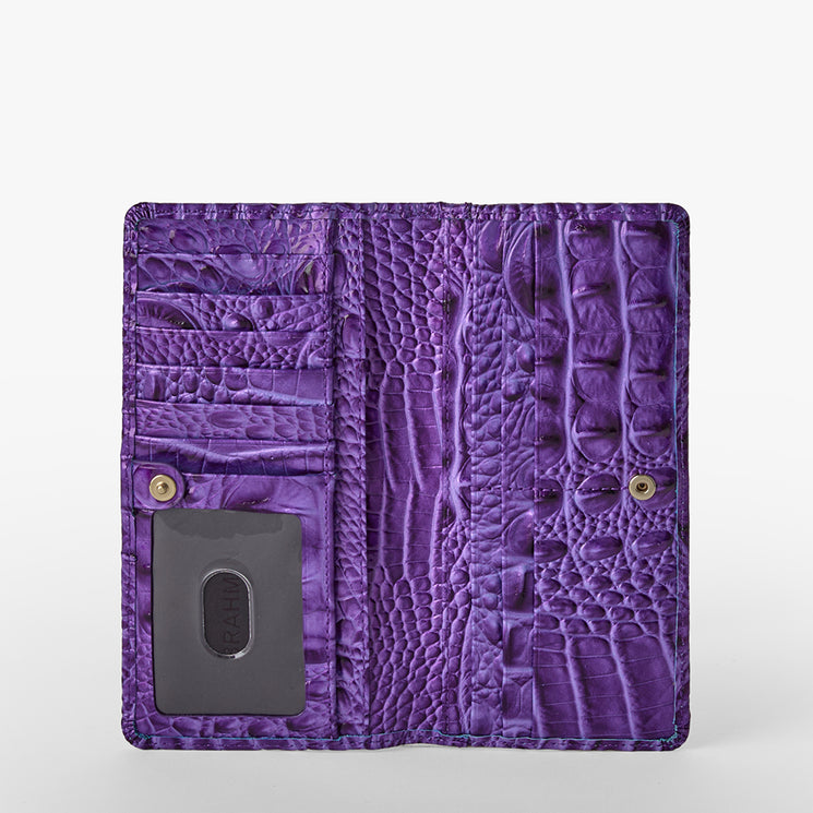 Brahmin purple embossed leather wallet open to show multiple card slots, a clear ID window, and dual snap button closures. Crocodile-inspired textured pattern enhances the structured rectangular silhouette.