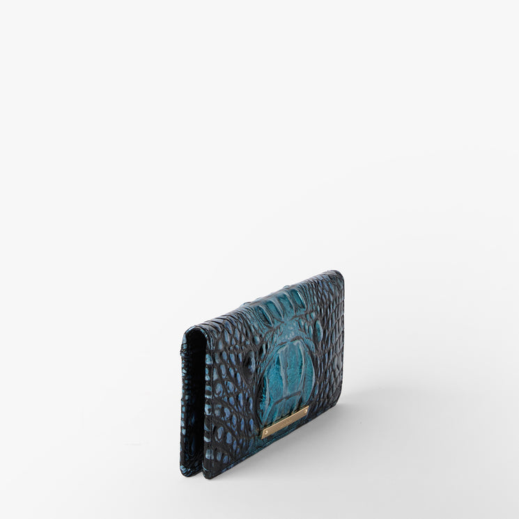 Brahmin blue textured wallet with embossed pattern, small gold nameplate, and structured silhouette shown standing slightly open on a white background. Interior details partially visible near top opening.
