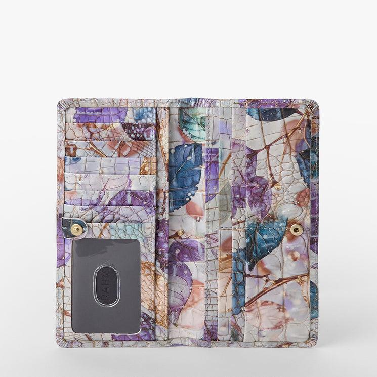 Brahmin colorful wallet with purple, blue, and beige leaf pattern; bi-fold silhouette open to reveal card slots, clear ID window, multiple compartments; shown against a white background.