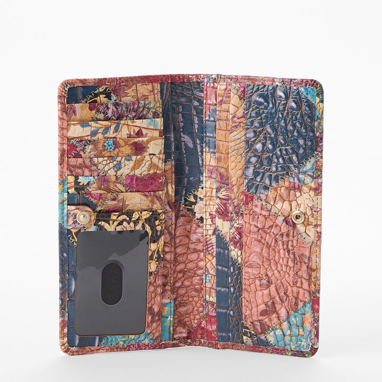 Brahmin wallet with patchwork embossed texture in blue, tan, pink, and yellow. Shown open upright on white surface revealing card slots and clear ID window. Structured silhouette with vibrant pattern.