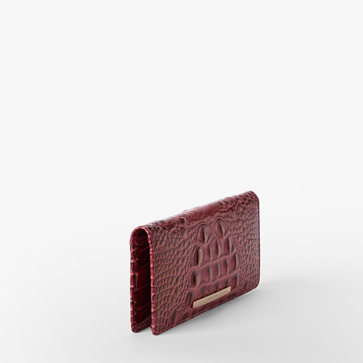 Brahmin burgundy textured leather wallet with gold nameplate hardware, standing upright against a plain white background, showcasing its structured silhouette and elegant finish.