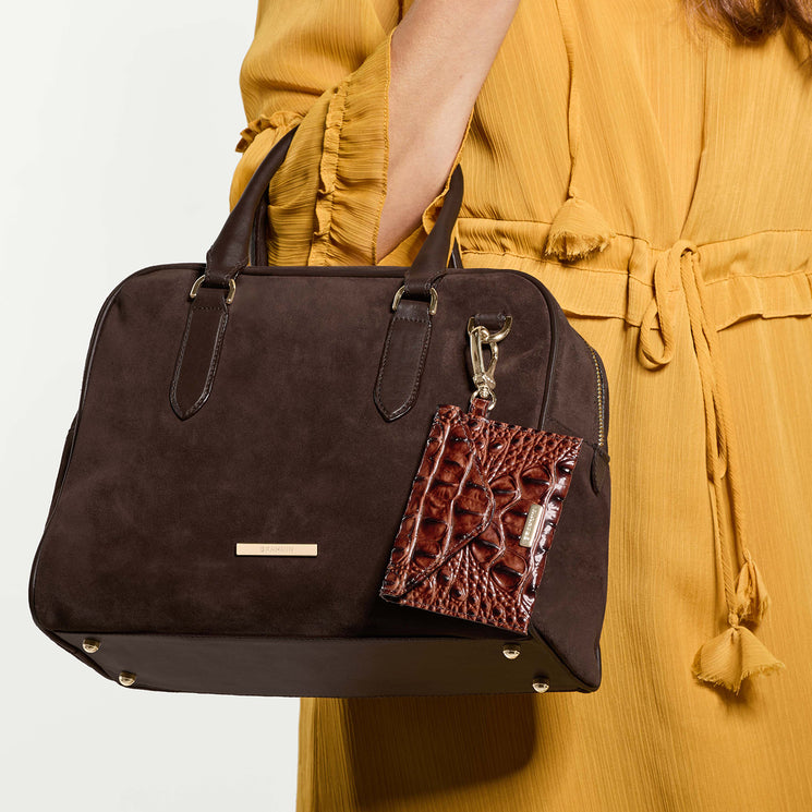 Brown handbag with a Envelope Pouch keychain held by a person wearing a yellow dress.