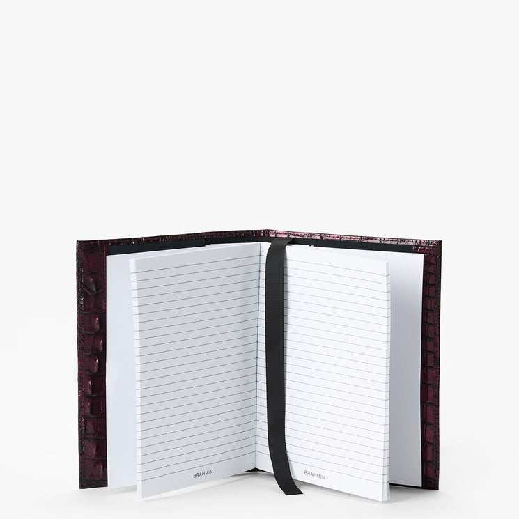 An open lined notebook with a dark textured cover and a black ribbon bookmark, photographed on a clean white background.
