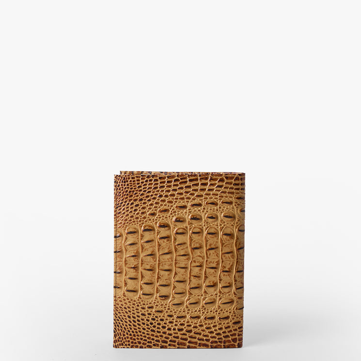 Brahmin brown embossed wallet with a textured scale-inspired pattern stands upright on a white background, front view highlighting detailed design and structured silhouette. No hardware or straps visible.