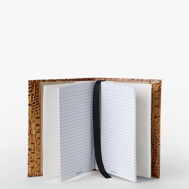 Brahmin notebook with lined pages, black ribbon bookmark, and a textured brown cover featuring an embossed pattern. Displayed open on a white background, highlighting interior details and luxury craftsmanship.