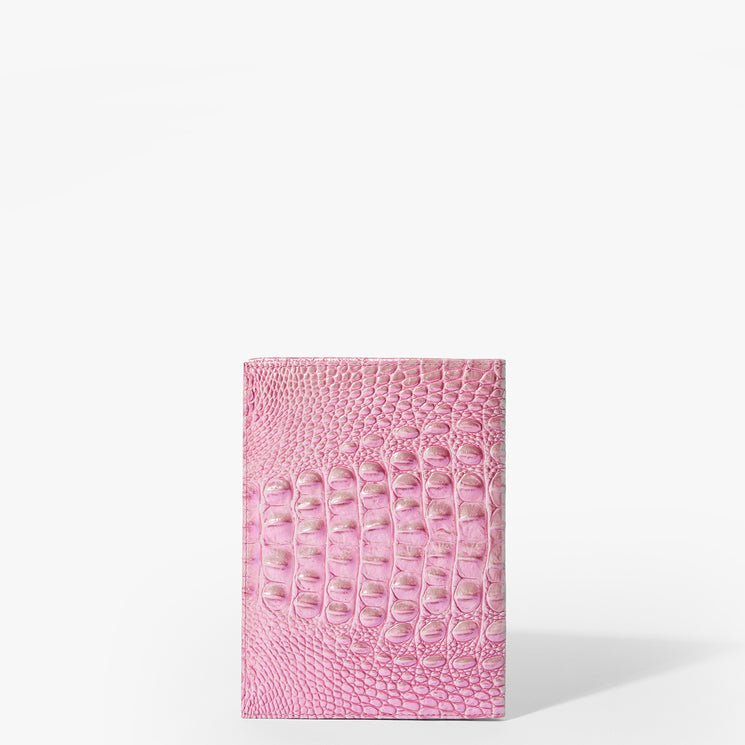 Brahmin pink embossed leather notebook standing upright on a white background, featuring a structured silhouette and textured pattern with no visible hardware or strap, casting a soft shadow to the right.