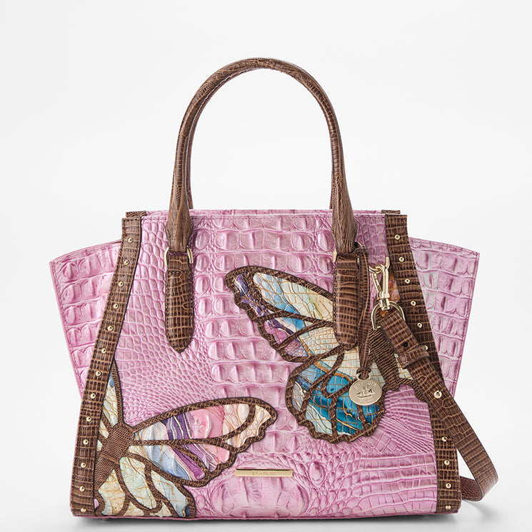 Brahmin pink embossed handbag with brown handles and trim, featuring colorful butterfly motifs, gold-tone hardware including a keychain charm and metal studs. Structured silhouette shown from the front.