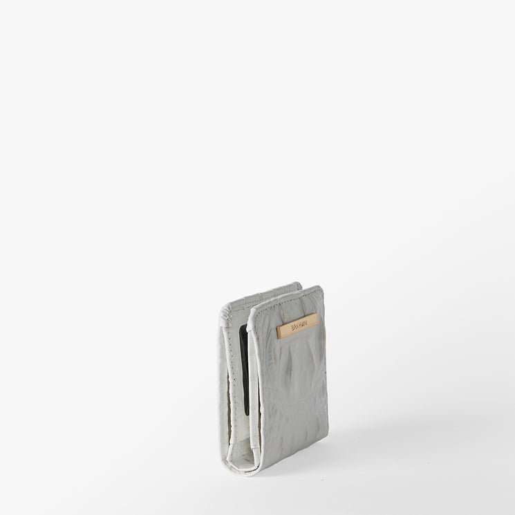 Brahmin light gray minimalist wallet stands upright on a white background. Features a beige card in one slot, slim silhouette, clean lines, and subtle embossed Brahmin logo. Simple, elegant accessory view.