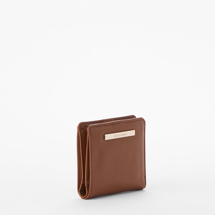 A brown leather bi-fold wallet with a small gold-tone metal brand plaque on the front, standing upright on a clean white background.