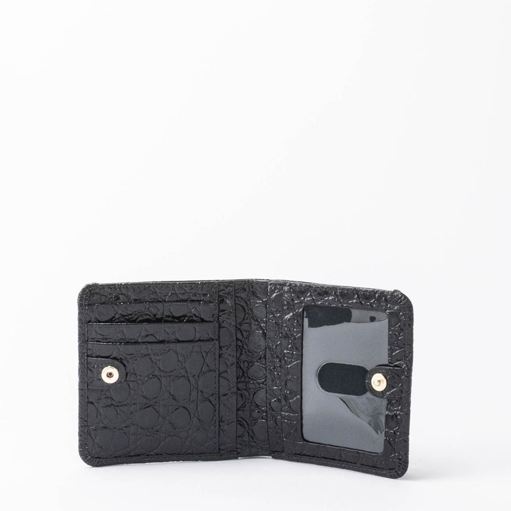 BRAHMIN Jane mini wallet in black leather shown open with card slots, a buttoned coin pocket, and a tab ID window. Compact silhouette with smooth texture, displayed on a white background.