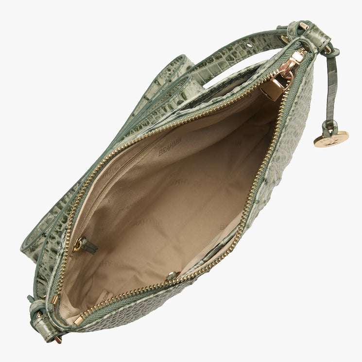 An open green crocodile-embossed leather bag with a beige interior lining and gold-tone hardware, shown on a light gray background.