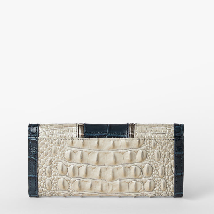 Brahmin rectangular clutch purse with cream embossed pattern, dark blue trim, structured silhouette, metal top handle, and sleek design displayed on a white background.