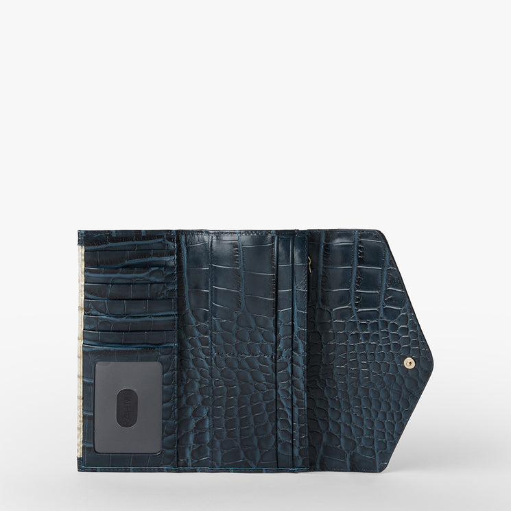 Brahmin dark blue embossed wallet open to show card slots, clear ID window, snap button flap closure, and textured finish. Silhouette displayed on a white background. No strap visible in this view.