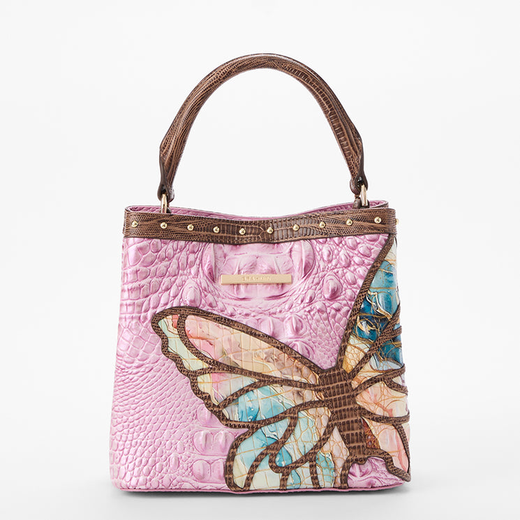 Brahmin pink textured satchel with brown handles, structured silhouette, gold-tone hardware, and a bold butterfly motif in brown, blue, yellow, and beige. Front view; top handles shown.