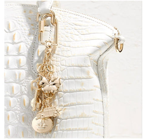 White crocodile-embossed leather handbag detail with gold hardware and decorative charm accents.