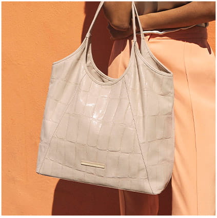 Light neutral crocodile-embossed leather tote bag worn over the shoulder against a warm-toned background.