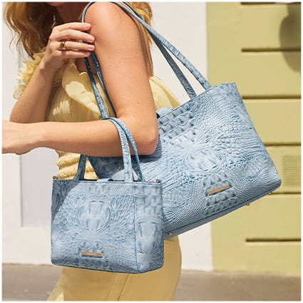 Light blue crocodile-embossed leather tote and matching mini bag carried together by a model.